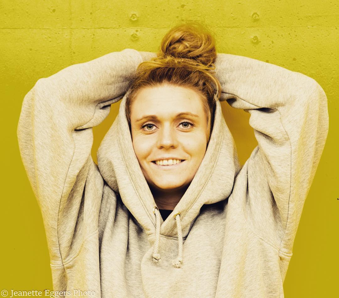 Graduate Carolie Gudmundsson in a grey hoodie against a yellow wall
